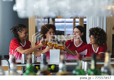 Diverse group of male and female sports fans raising glasses and watching game at bar 77557857