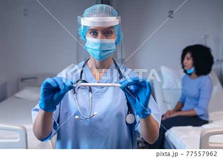 Caucasian female doctor in hospital wearing face mask and surgical gloves holding swab test 77557962