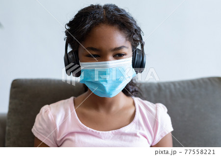 Portrait of mixed race girl wearing face mask and headphones Portrait of mixed race girl wearing face mask and headphones 77558221