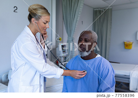 Caucasian female doctor examining with stethoscope african american male patient in hospital room Caucasian female doctor examining with stethoscope african american male patient in hospital room 77558396