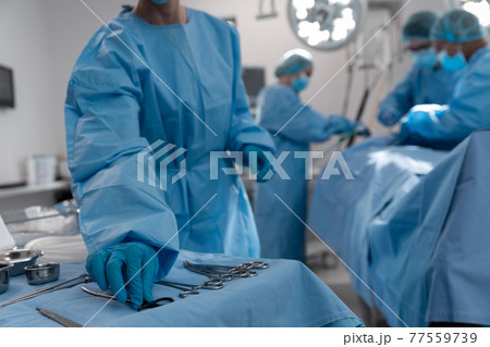 Midsection of female surgeon reaching for surgical scissors in operating theatre Midsection of female surgeon reaching for surgical scissors in operating theatre 77559739