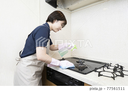 ガスレンジの清掃をするハウスクリーニングの女性作業員 77561511
