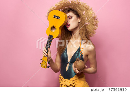 Woman holding ukulele coconut cocktail beach hat Exotic lifestyle swimsuit pink background 77561959