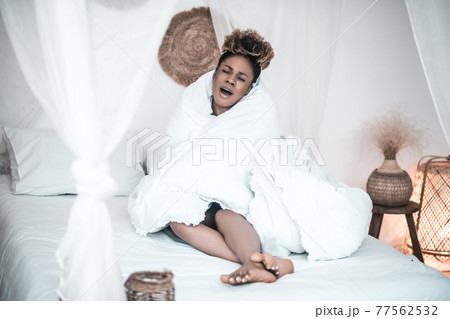 Woman with closed eyes sitting in blanket Woman with closed eyes sitting in blanket 77562532