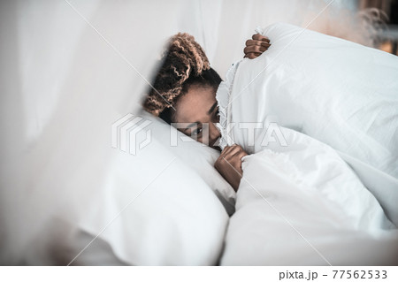 Sleepy woman peeking out from under blanket Sleepy woman peeking out from under blanket 77562533