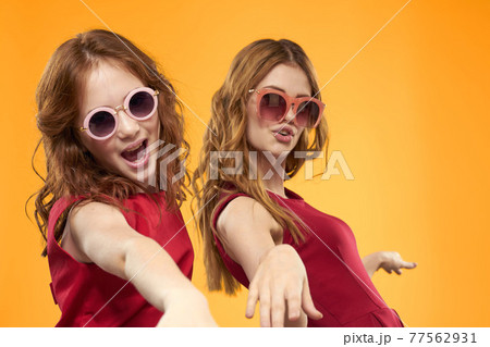 Happy sisters in red dresses on a yellow background are having fun and gesticulating Copy Space 77562931