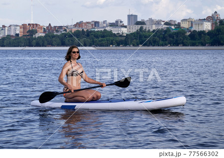 A beautiful woman is engaged in summer active sports on the river on a SUP board A beautiful woman is engaged in summer active sports on the river on a SUP board 77566302