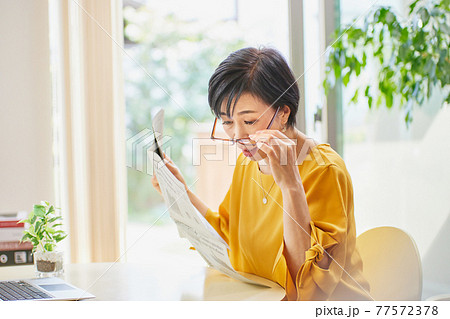 老眼鏡を掛けて英字新聞を読むミドル女性 77572378