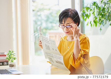 老眼鏡を掛けて英字新聞を読むミドル女性 老眼鏡を掛けて英字新聞を読むミドル女性 77572379