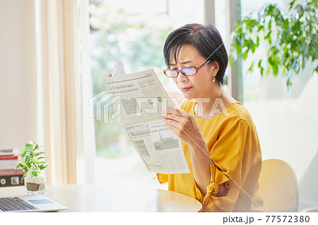老眼鏡を掛けて英字新聞を読むミドル女性 老眼鏡を掛けて英字新聞を読むミドル女性 77572380