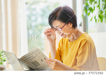 老眼鏡を掛けて英字新聞を読むミドル女性 77572392