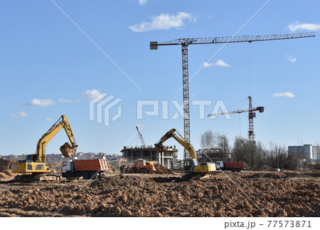 Excavator digging sand and loading into dump truck on construction site.  77573871