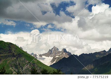 High rocky mountains with snow and glacier, sunlit blue sky with clouds at summer evening 77575219
