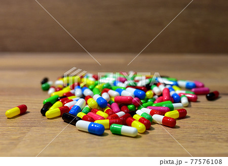 Pills in multicolored capsules on wooden background.  77576108