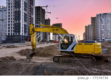 Excavator during earthmoving work at construction site on sunset background. Excavator during earthmoving work at construction site on sunset background. 77576736