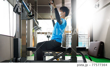 マスクをつけてウエイトトレーニングをする若い男性 77577364