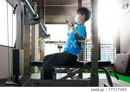 マスクをつけてウエイトトレーニングをする若い男性 77577365
