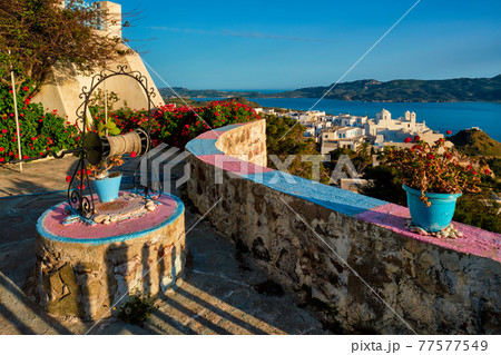 Picturesque scenic view of Greek town Plaka on Milos island over red geranium flowers 77577549