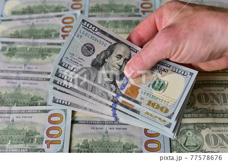 Stack Of 100 Dollars Banknotes Bundles in a man's hand against the background of American banknotes Stack Of 100 Dollars Banknotes Bundles in a man's hand against the background of American banknotes 77578676