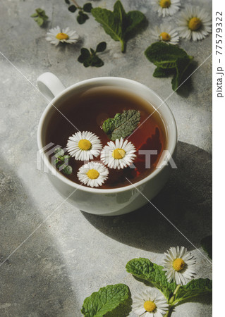 Cup of herbal tea with chamomile flowers and mint leaves Cup of herbal tea with chamomile flowers and mint leaves 77579322