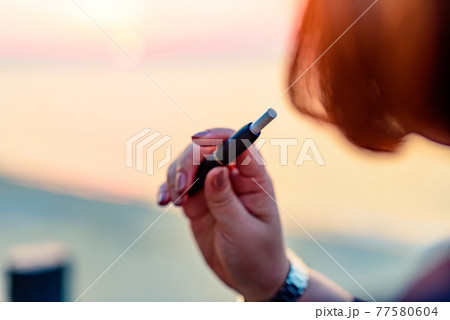 加熱式たばこを吸う女性　色味青寄り 77580604