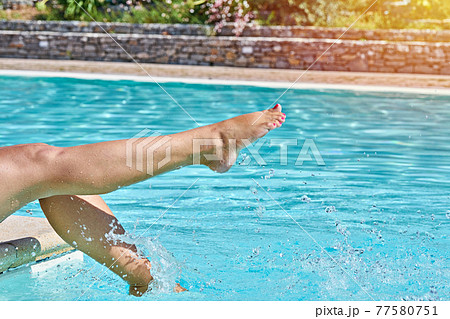 Female barefoot legs in pool splashing in sunlight in motion. Summertime moments concept Female barefoot legs in pool splashing in sunlight in motion. Summertime moments concept 77580751