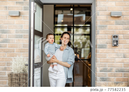 Housewife with newborn baby staying in front of entrance door 77582235