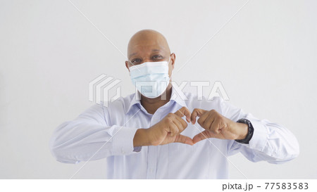 Old elderly black business man. Sick African American person wearing a face mask and making heart symbol in medical treatment and health care isolated on white. Coronavirus. People lifestyle activity. 77583583