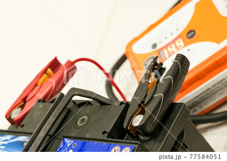 Recharging the car battery with red and black copper clips attached to the terminals. 77584051