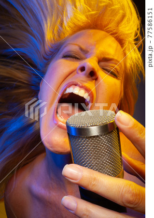 Female vocalist under gelled lighting sings with passion into condenser microphone. Female vocalist under gelled lighting sings with passion into condenser microphone. 77586151