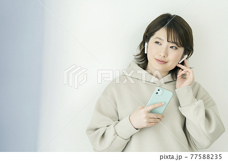 ヘッドホンをしてスマホを持つ笑顔の若い女性 ヘッドホンをしてスマホを持つ笑顔の若い女性 77588235