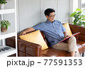 senior asian man reading book on sofa 77591353