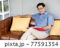 senior asian man reading book on sofa 77591354