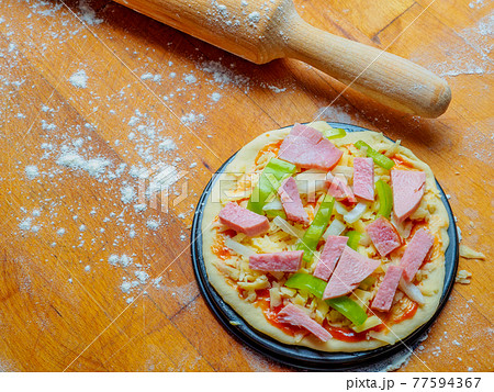 Pizza on a wooden table sprinkled with flour. 77594367