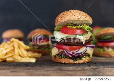 Double Hamburger with tomatoes, onions, cucumber, lettuce , melting cheese and french fries  served on a  rustic wooden table 77597251