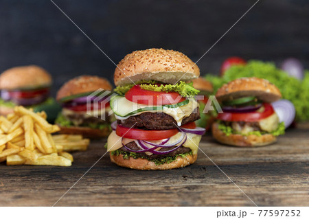 Double Hamburger with tomatoes, onions, cucumber, lettuce , melting cheese and french fries  served on a  rustic wooden table 77597252