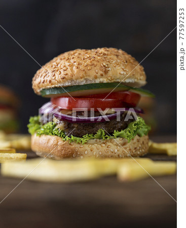 Hamburger with tomatoes, onions, cucumber, lettuce , melting cheese and french fries served on a  rustic wooden table 77597253