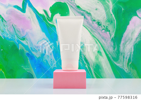 Hands cream in white unbranded tube on pink podium against bright marbled background with copy space 77598316