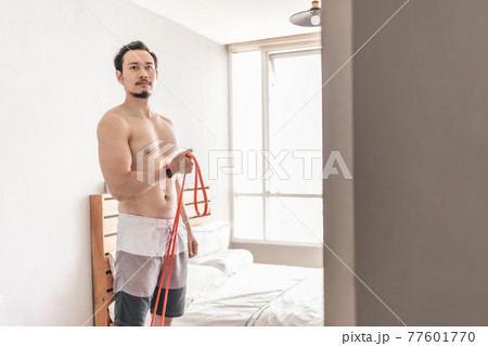 Man stretching his muscle in concept of workout at home with resistance band. Man stretching his muscle in concept of workout at home with resistance band. 77601770