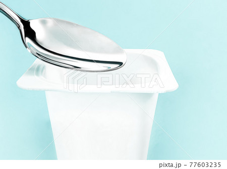 Yogurt cup and silver spoon on mint background, white plastic container with yoghurt cream, fresh dairy product for healthy diet and nutrition balance 77603235
