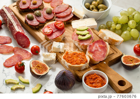 Assortment of sausages and cheese, salami, grapes, baguette slices, olives, on white background. Close up Assortment of sausages and cheese, salami, grapes, baguette slices, olives, on white background. Close up 77603676