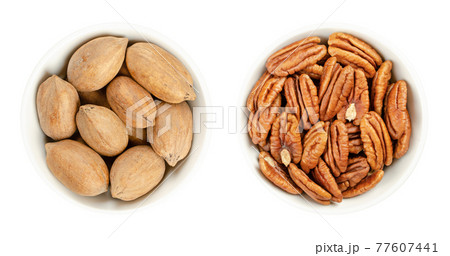 Pecan nuts, shelled and unshelled, in white bowls. Whole pecans and pecan halves, seeds and edible nuts of Carya illinoinensis, used as snack. Close-up from above isolated over white macro food photo. 77607441