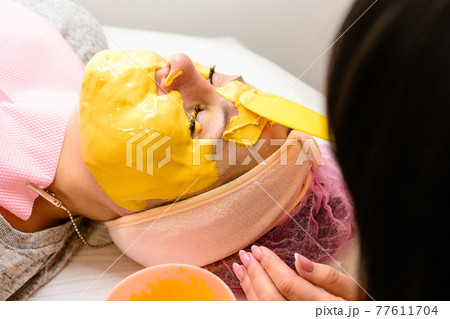 Woman at the beautician applying a relaxing golden mask on the face, restoring and moisturizing the skin. 77611704