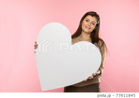 Girl with a large white heart shape in the hands. A student in love stands and holds a large heart shape in her hands. Valentine's Day and love. Girl with a large white heart shape in the hands. A student in love stands and holds a large heart shape in her hands. Valentine's Day and love. 77611845