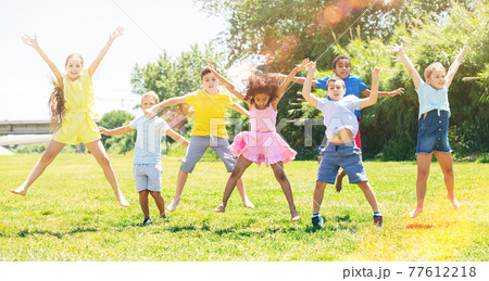 Schoolchildren jumping and smiling together in park 77612218
