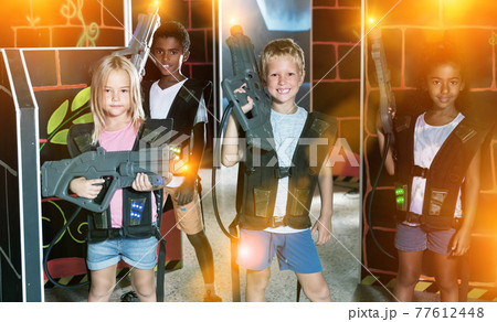 Group of glad pleasant teenagers with laser guns having fun on dark lasertag arena 77612448