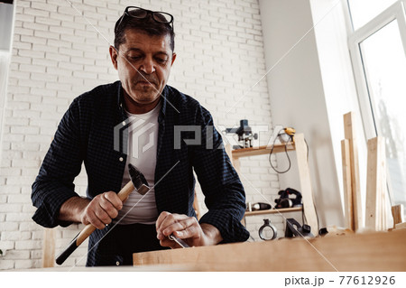 Middle-aged man carpenter working in a workshop with chisel and hammer 77612926