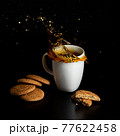 Glass with tea pouring with liquid with splashes and drops of water. Brewing tea concept. Cup pouring with water or tea with splashes on dark wooden background. Cup, teabag and cookies on table. 77622458