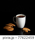 Glass with tea pouring with liquid with splashes and drops of water. Brewing tea concept. Cup pouring with water or tea with splashes on dark wooden background. Cup, teabag and cookies on table. 77622459