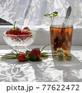 Cup of tea and wild strawberries on a white lace background 77622472